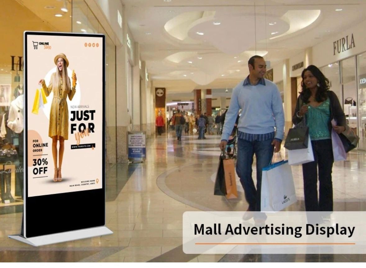 Digital advertising display in a mall promoting a sale with people walking and shopping in the background.